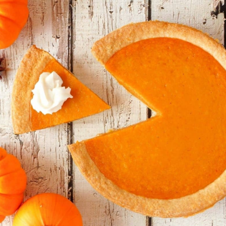 Whole pumpkin pie on a wooden table before being cut into pumpkin pie bites