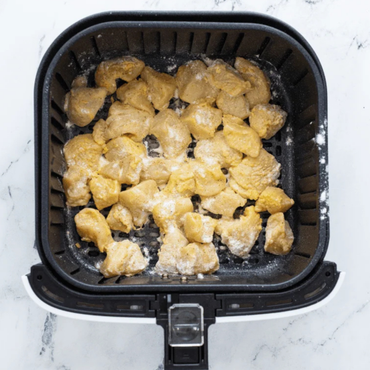 Raw chicken nuggets coated in seasoned flour resting on parchment paper, ready for air frying after dredging.