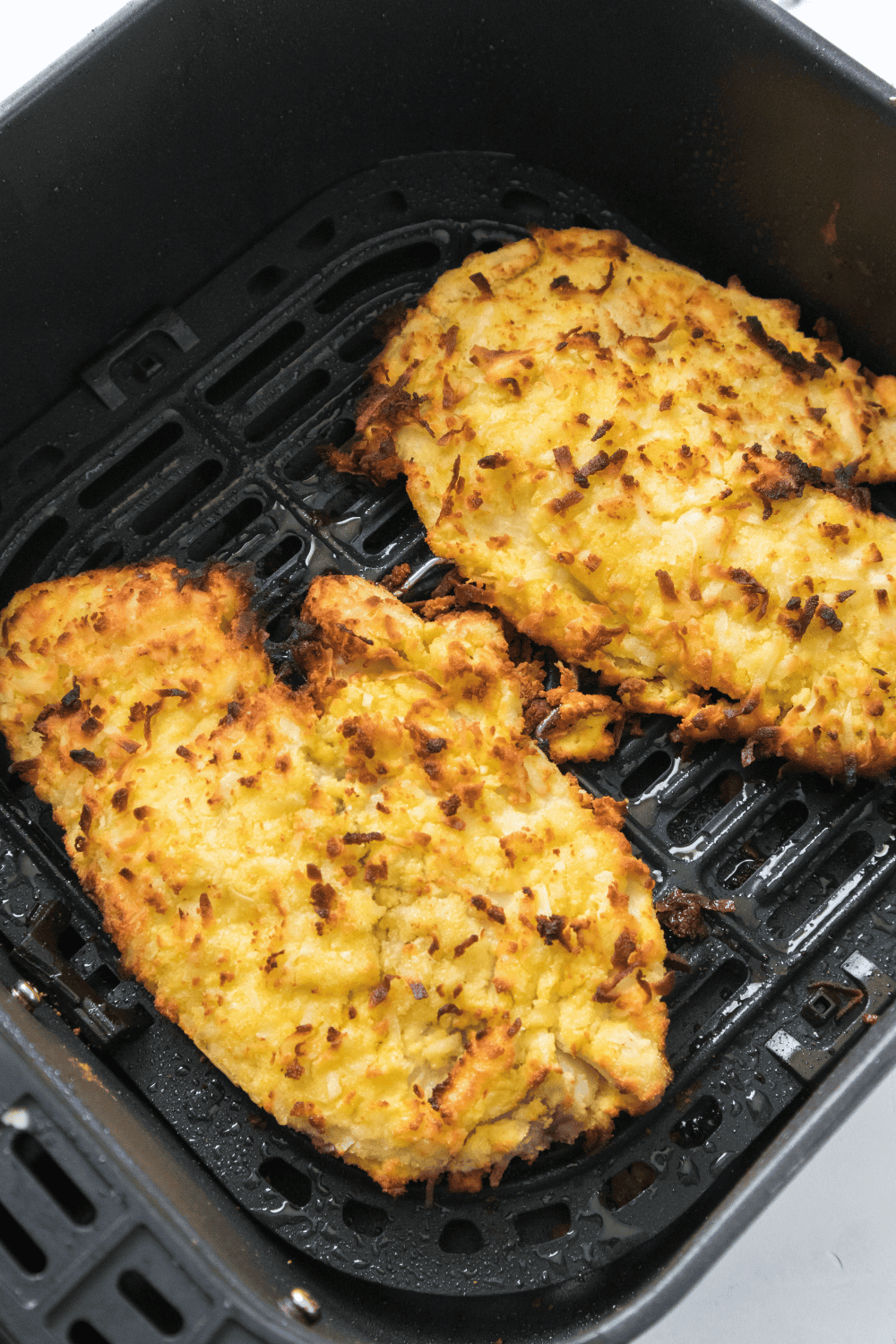 Crispy air fryer coconut crusted tilapia fillet with golden coating, served with fresh herbs and lemon slices