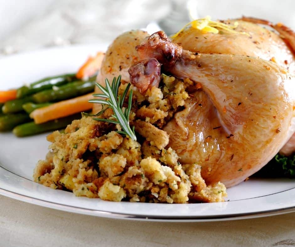 Cornish hen with stuffing and sprig of rosemary on a plate. 