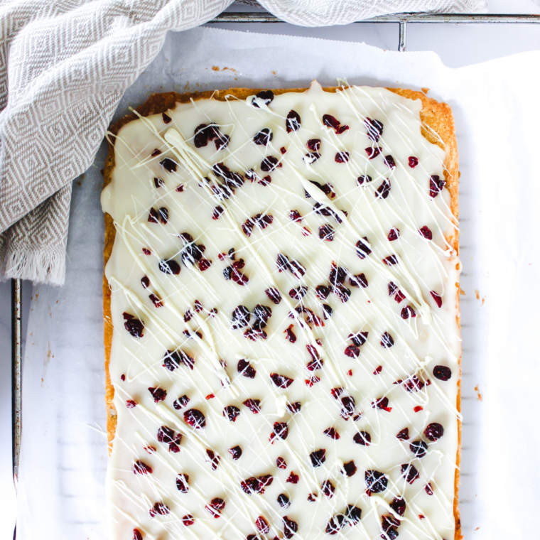 Air fryer cranberry bliss bars cut into triangles, topped with orange cream cheese frosting, dried cranberries, and white chocolate drizzle