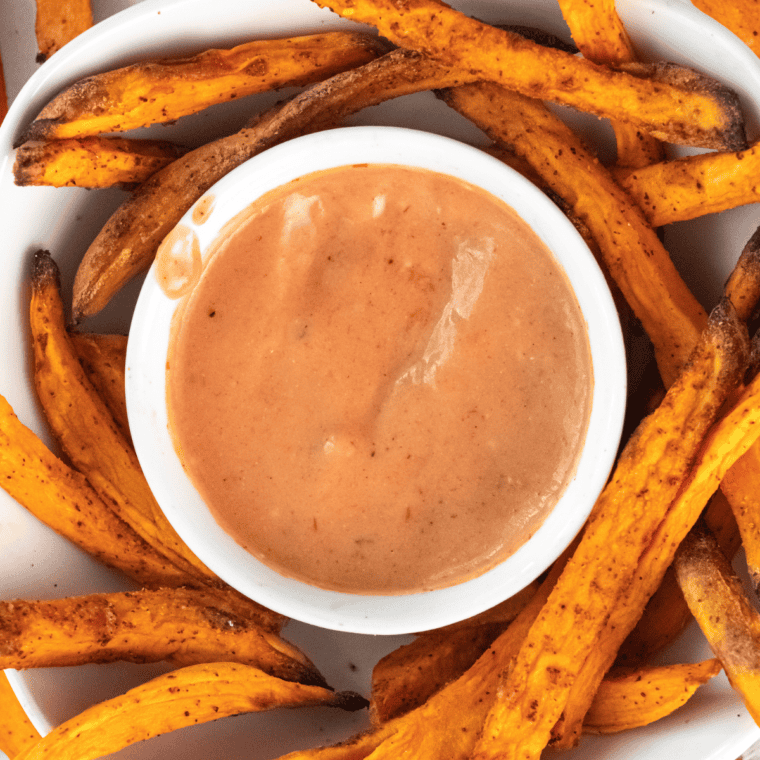 Bowl of Air Fryer Frozen Sweet Potato Fries with dipping sauce in the middle of the plate.