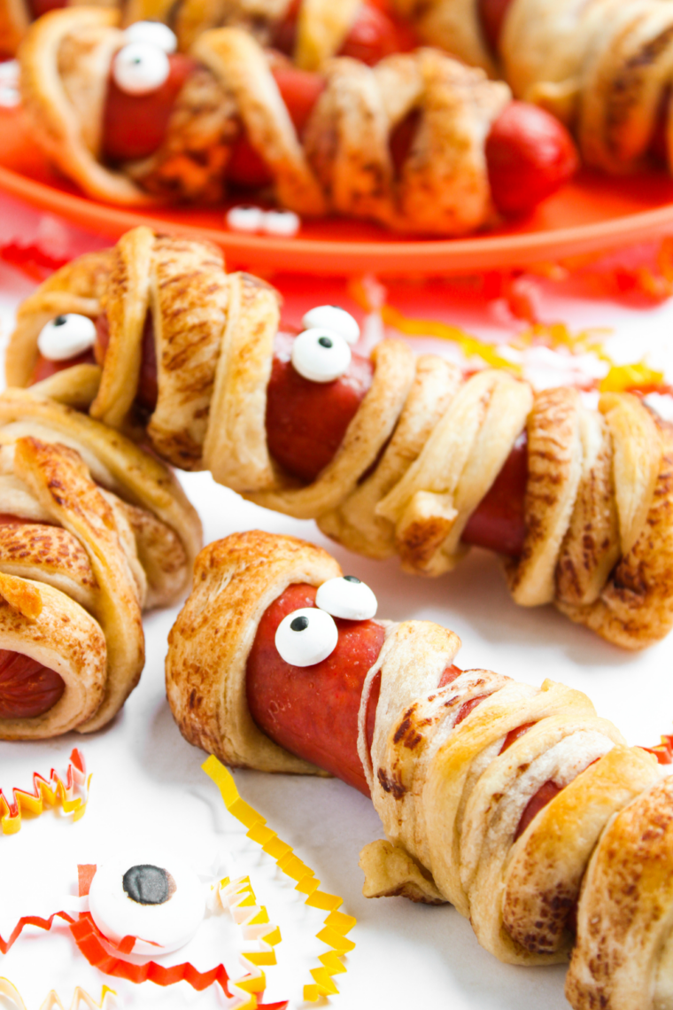 Air fryer mummy hot dogs wrapped in crescent dough with candy eyeballs, cooked until golden brown and crispy for a Halloween snack.