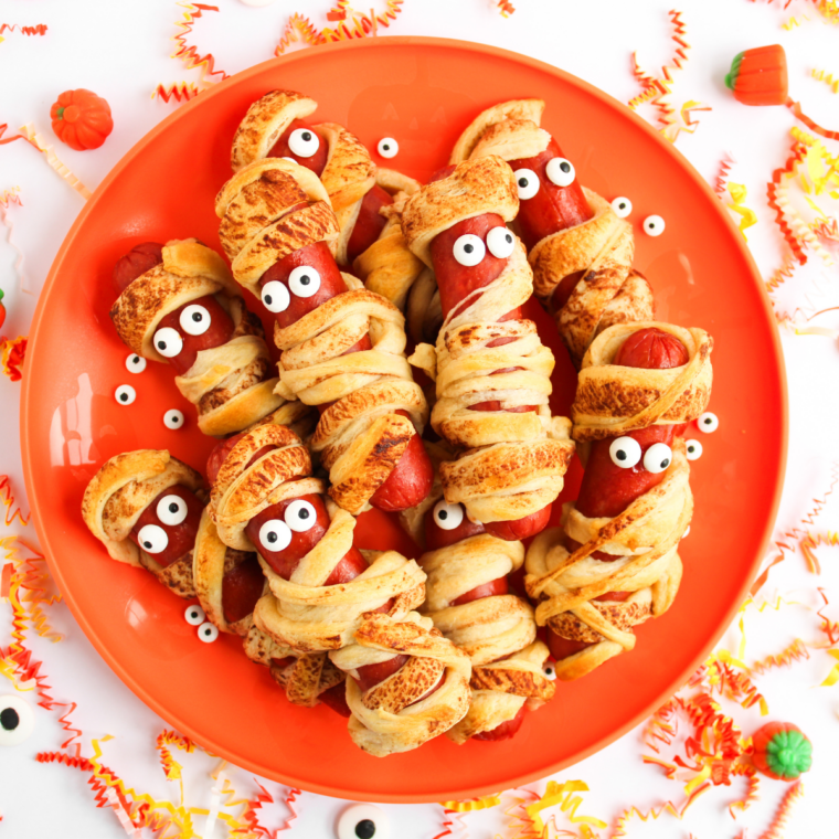 Air fryer mummy hot dogs wrapped in crescent dough with candy eyeballs, cooked until golden brown and crispy for a Halloween snack.