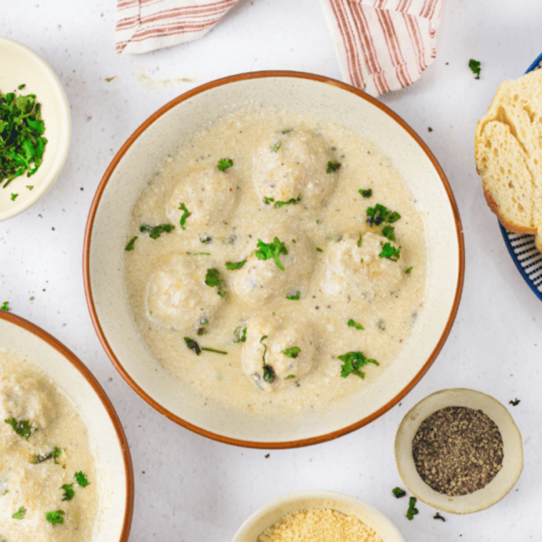 Close-up of meatballs in creamy Alfredo sauce topped with grated parmesan and herbs.