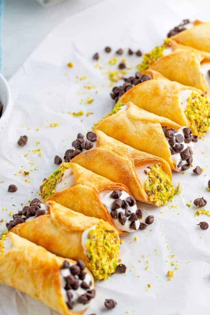 a row of air fried cannoli with chocolate chip and pistachio toppings