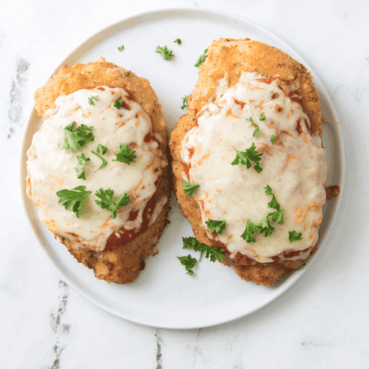 Air fryer crispy chicken parmesan topped with marinara sauce and melted mozzarella cheese on a white plate with fresh basil garnish.