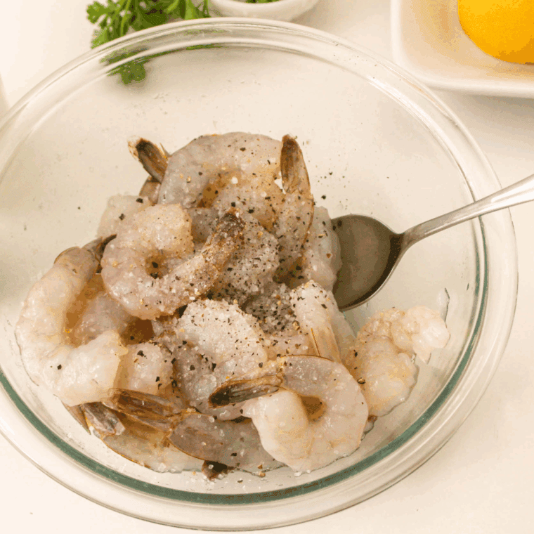 Raw shrimp being patted dry with paper towels and seasoned with salt and pepper.