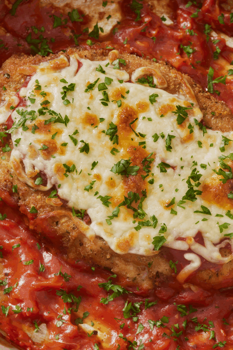 Crispy breaded chicken breast topped with marinara sauce and melted mozzarella cheese, served with fresh basil on a white plate—Carrabba’s Chicken Parmesan Recipe.