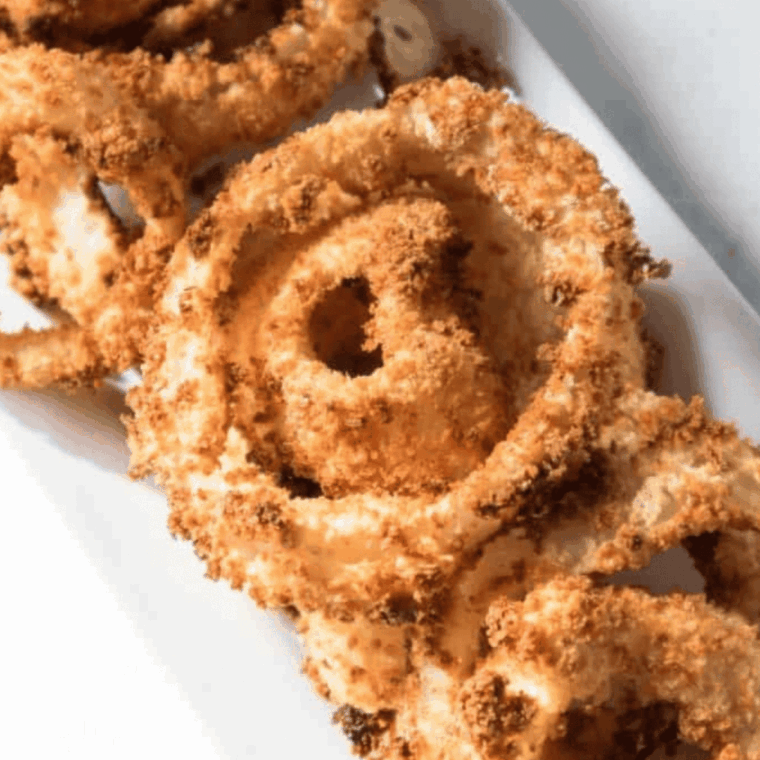 Extra crispy homemade onion rings stacked on a plate with dipping sauce