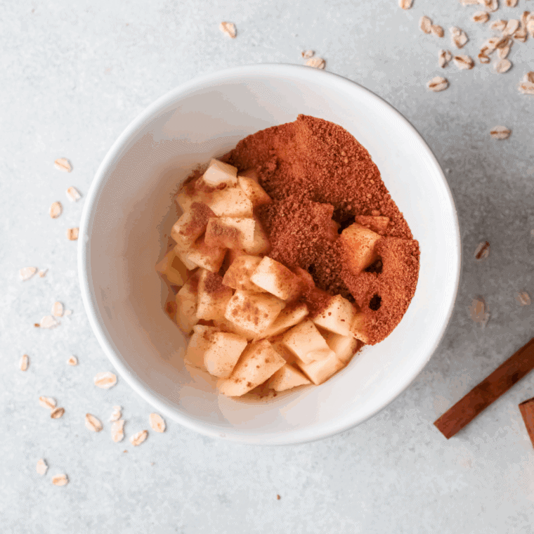 Sliced and peeled apples being tossed with granulated sugar, flour, cinnamon, and nutmeg in a 9x13 inch baking dish before being baked.