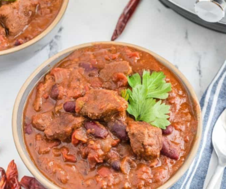 "A steaming bowl of Instant Pot Deer Chili topped with fresh cilantro and a dollop of sour cream."