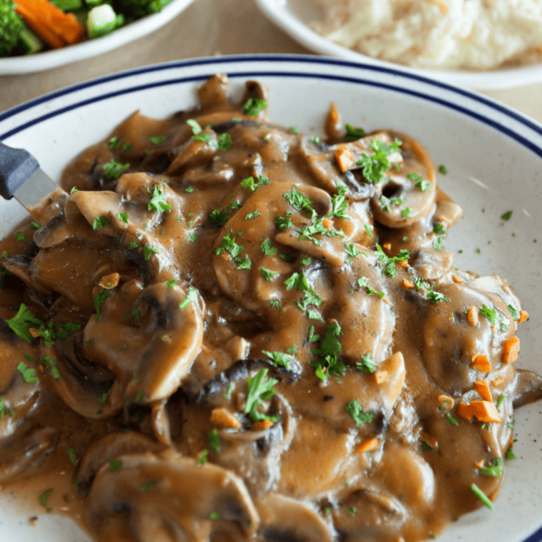 Cooked chicken breasts plated and topped with creamy Marsala sauce, garnished with parsley, ready to serve.
