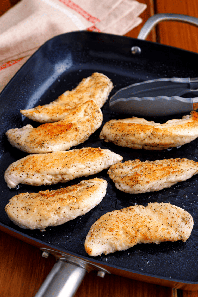 Chicken breasts searing in a skillet with olive oil and butter, golden brown on one side.