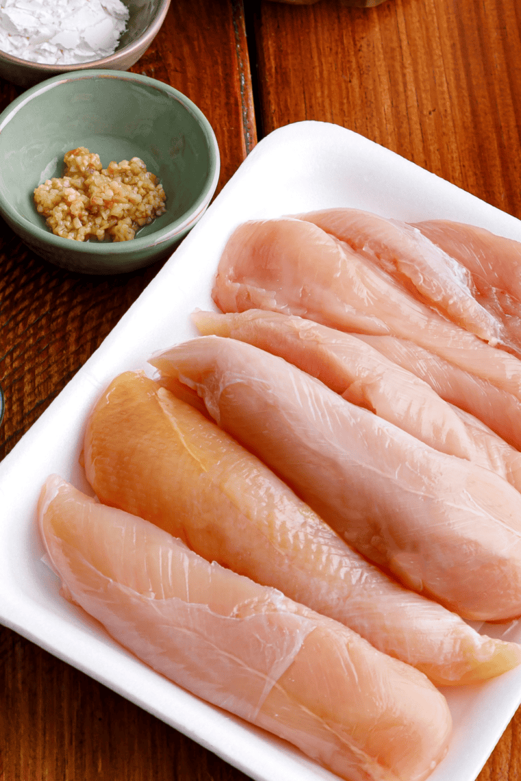 Raw chicken breasts seasoned with salt and pepper, dredged in flour on a cutting board.
