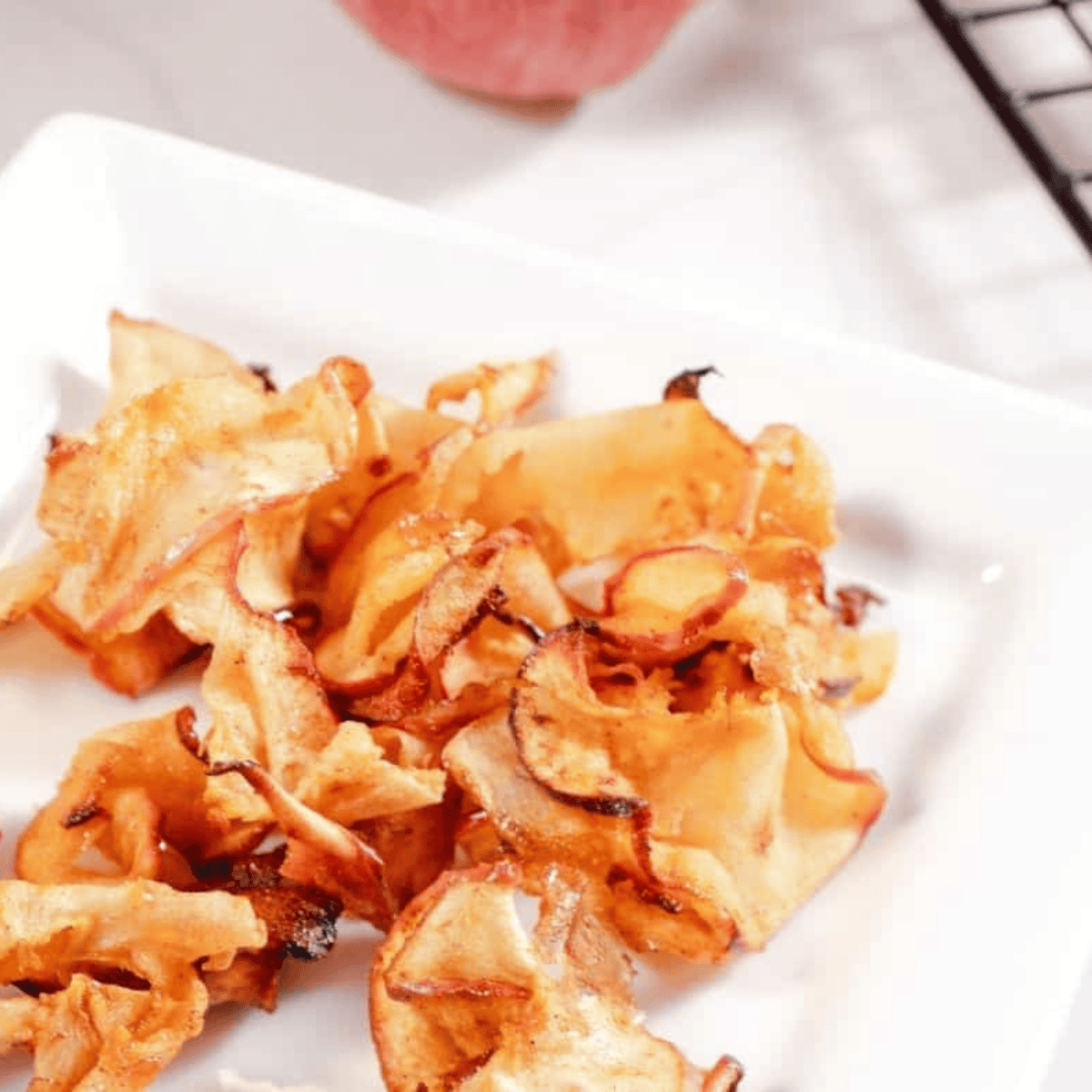 Thinly sliced apple chips crisping in an air fryer basket, golden brown and ready to eat.