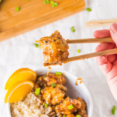 Slow cooker orange chicken served over white rice with sesame seeds and green onions