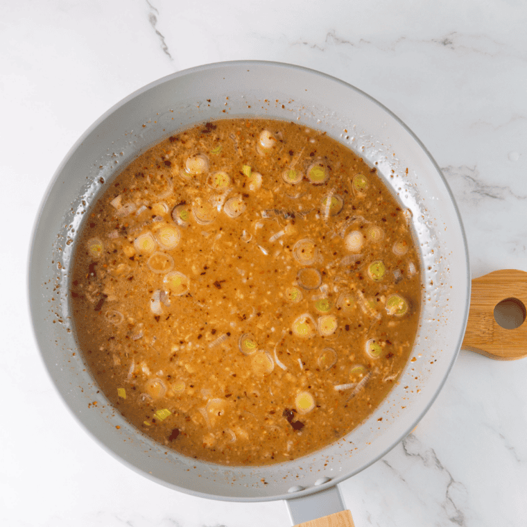 Whisking homemade orange chicken sauce with fresh orange juice, soy sauce, honey, garlic, and ginger in a glass bowl.