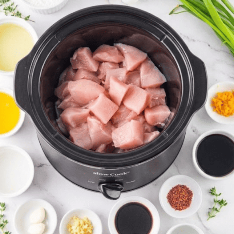 Chicken pieces coated in orange sauce in the slow cooker before cooking