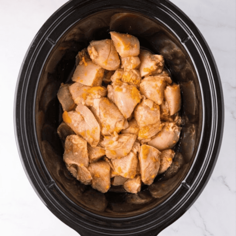 Stirring cornstarch slurry into crockpot orange chicken to thicken the glossy orange sauce.