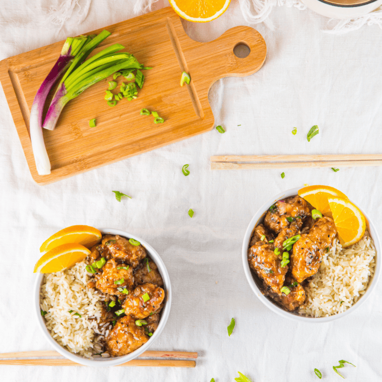 Slow cooker orange chicken served over steamed rice topped with sesame seeds and green onions