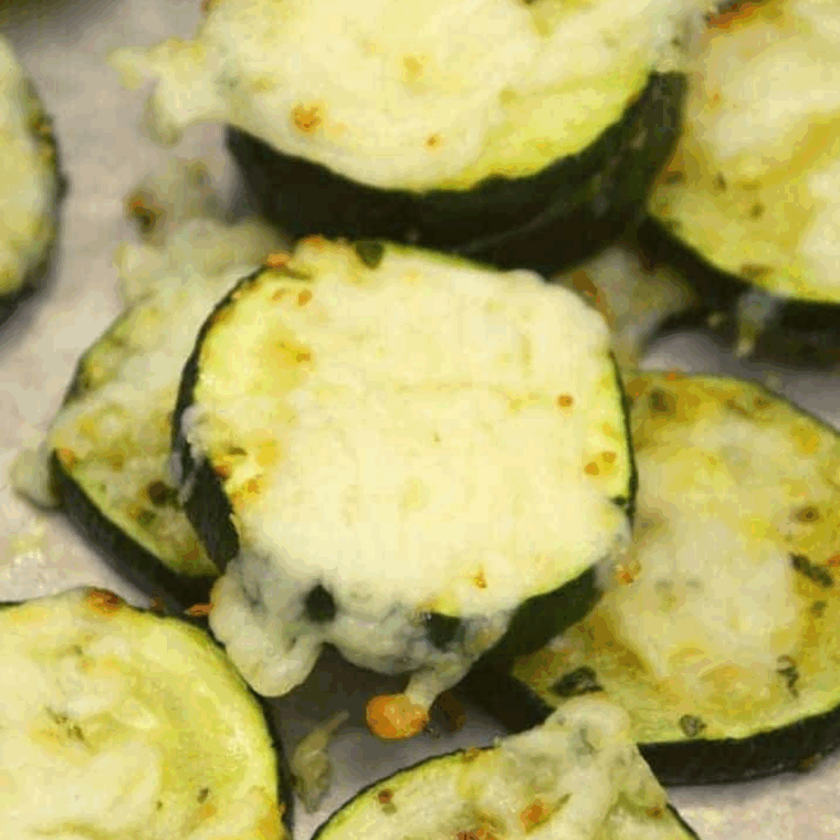 Golden air fryer zucchini slices topped with melted cheddar cheese, served on a white plate.