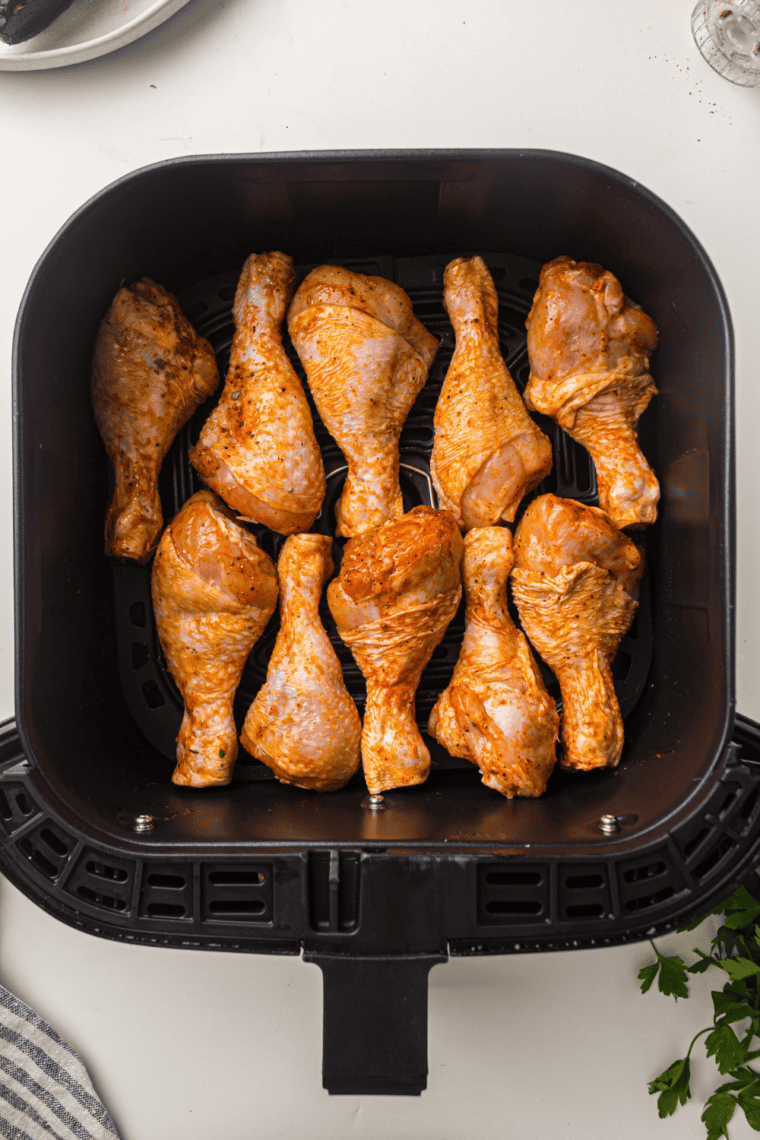 Placing seasoned frozen drumsticks in air fryer basket for cooking.