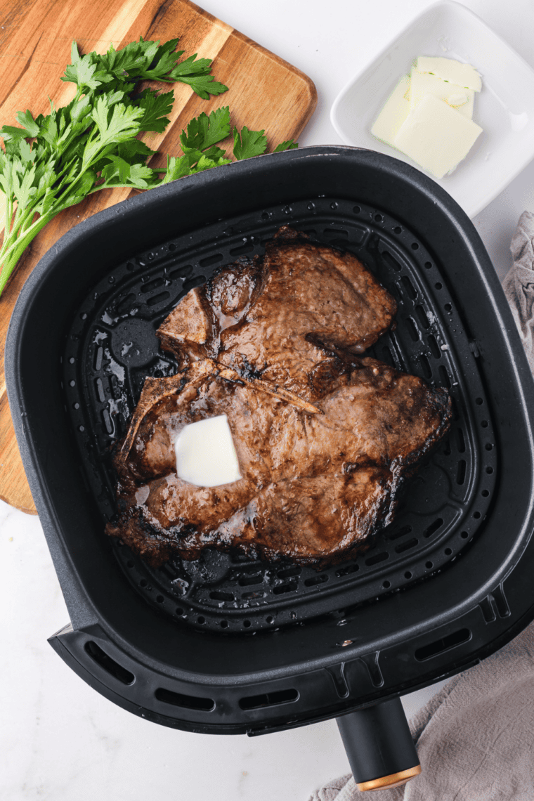 Air fryer porterhouse steak with a seared crust, sliced off the bone and topped with melting butter