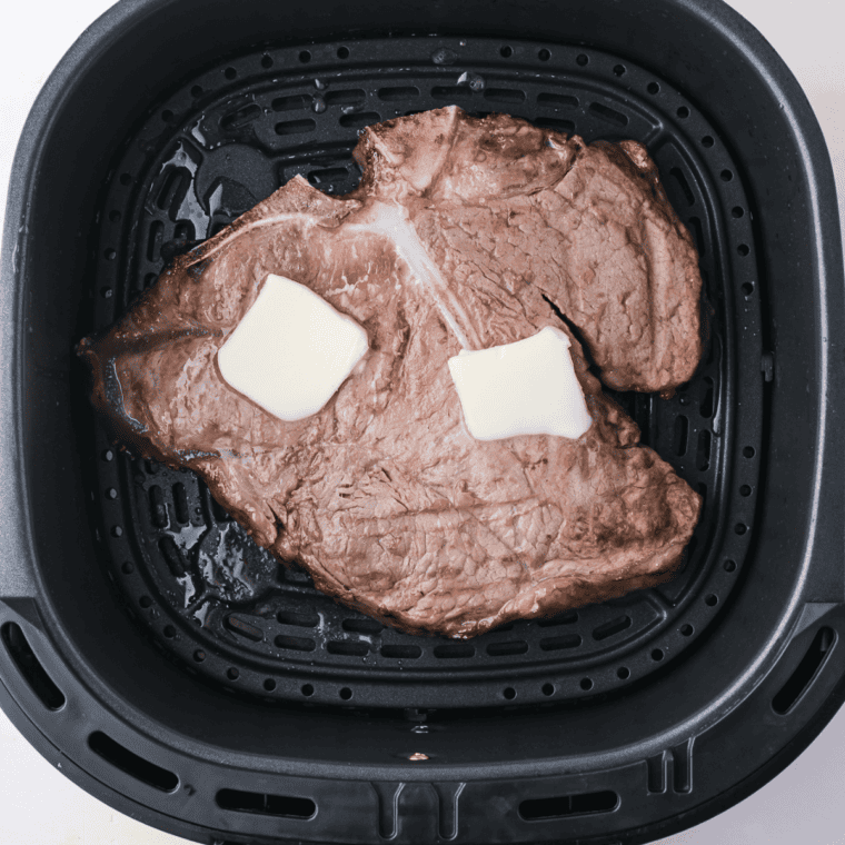 Two porterhouse steaks topped with butter cooking in a single layer in the air fryer basket