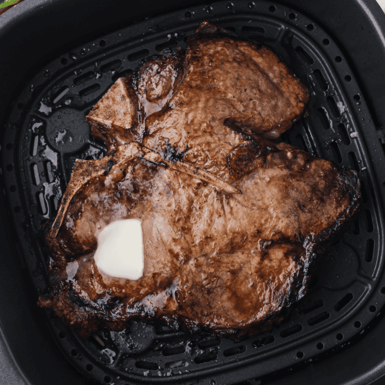 Juicy air fryer porterhouse steak sliced on a cutting board with garlic butter and fresh herbs.
