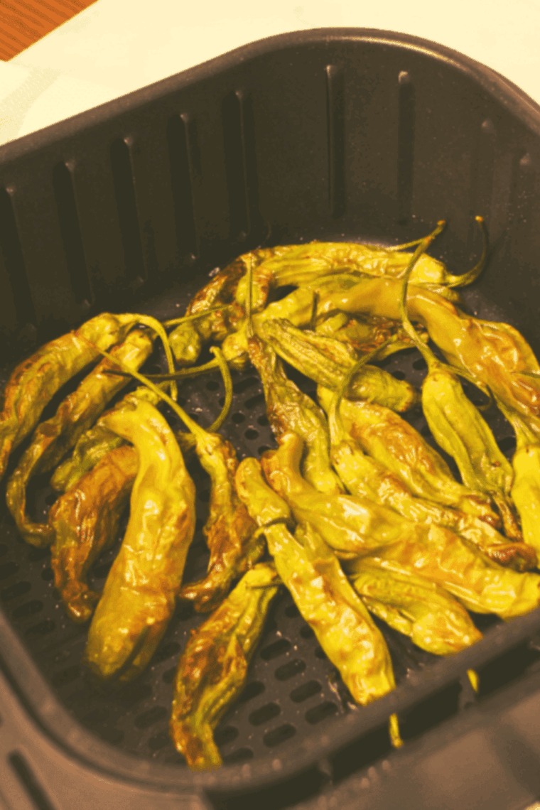 Shishito peppers arranged in an air fryer basket, cooking at 380°F until blistered and tender.