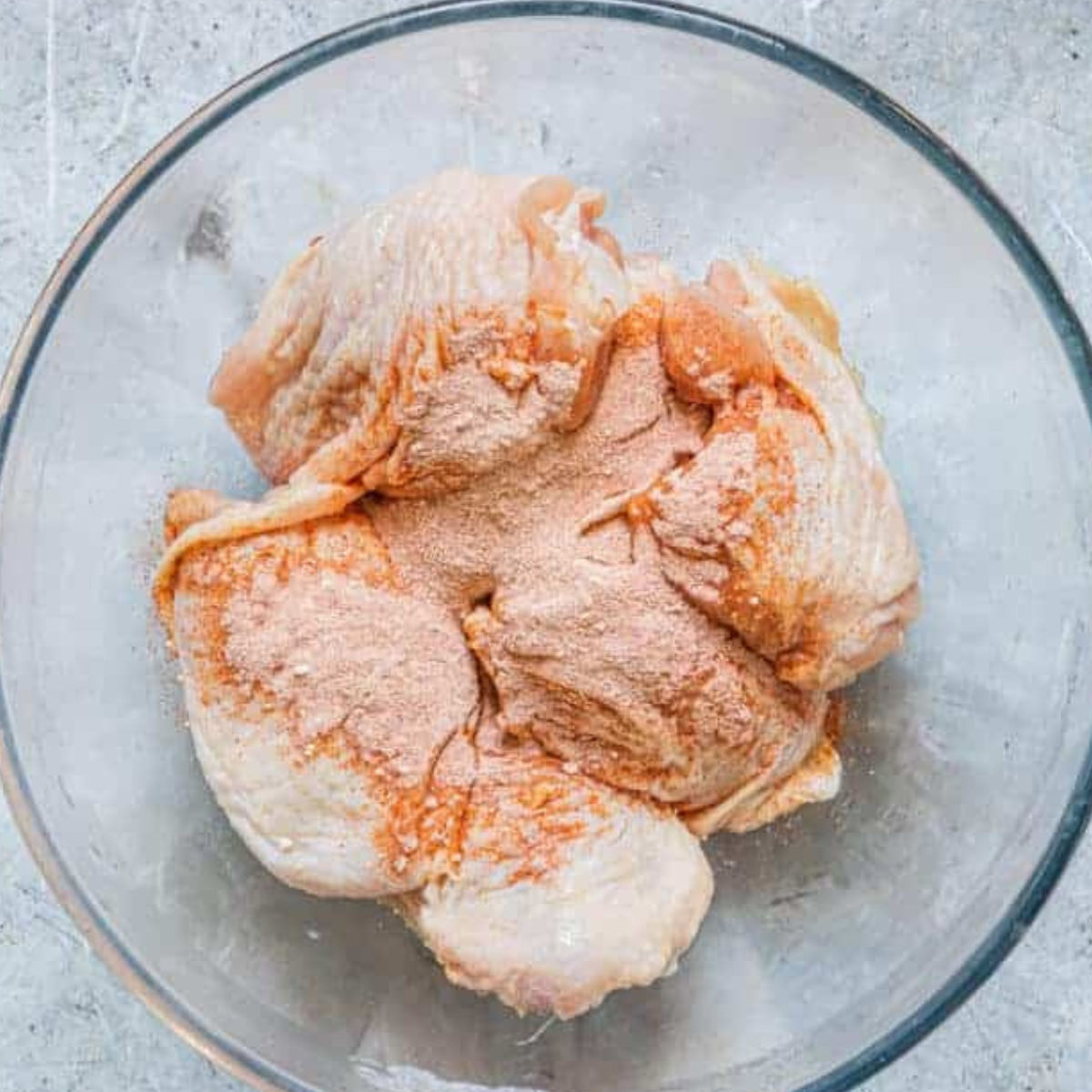 Bone-in chicken thighs being coated with brown sugar seasoning mix in a mixing bowl.