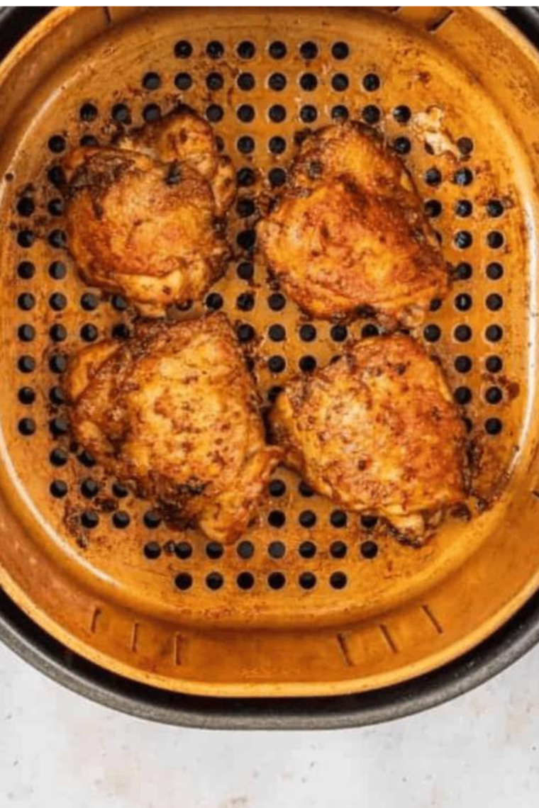 Air fryer basket filled with seasoned chicken thighs cooking to golden perfection.