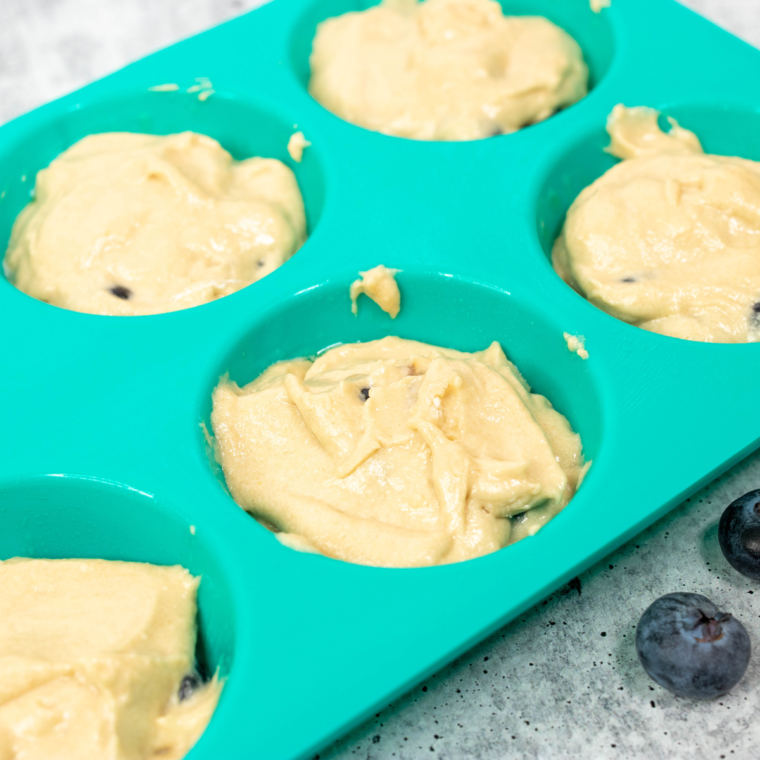 Pouring muffin batter into silicone cups or liners for Instant Pot Blueberry Muffins.