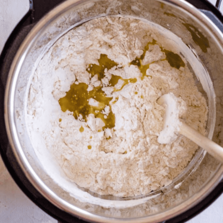 In the Instant Pot, combine the flour, salt, and yeast mixture. Start mixing with a wooden spoon. Add the olive oil and continue stirring. Little by little, add the remaining water. Mix until a soft and not too sticky dough forms. Knead it with a hand shortly to make sure all the flour is evenly absorbed.