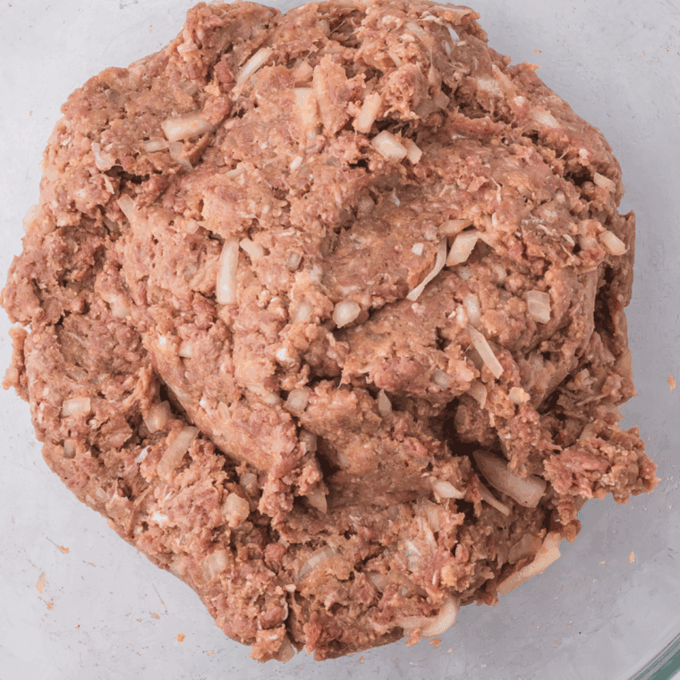 Mixing ground beef, eggs, onions, tomato sauce, crushed saltines, Cheddar cheese, Worcestershire sauce, and seasonings in a large bowl for Joanna Gaines meatloaf recipe.