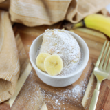 Golden air fryer banana bread mug cake in a white ramekin, topped with a banana slice
