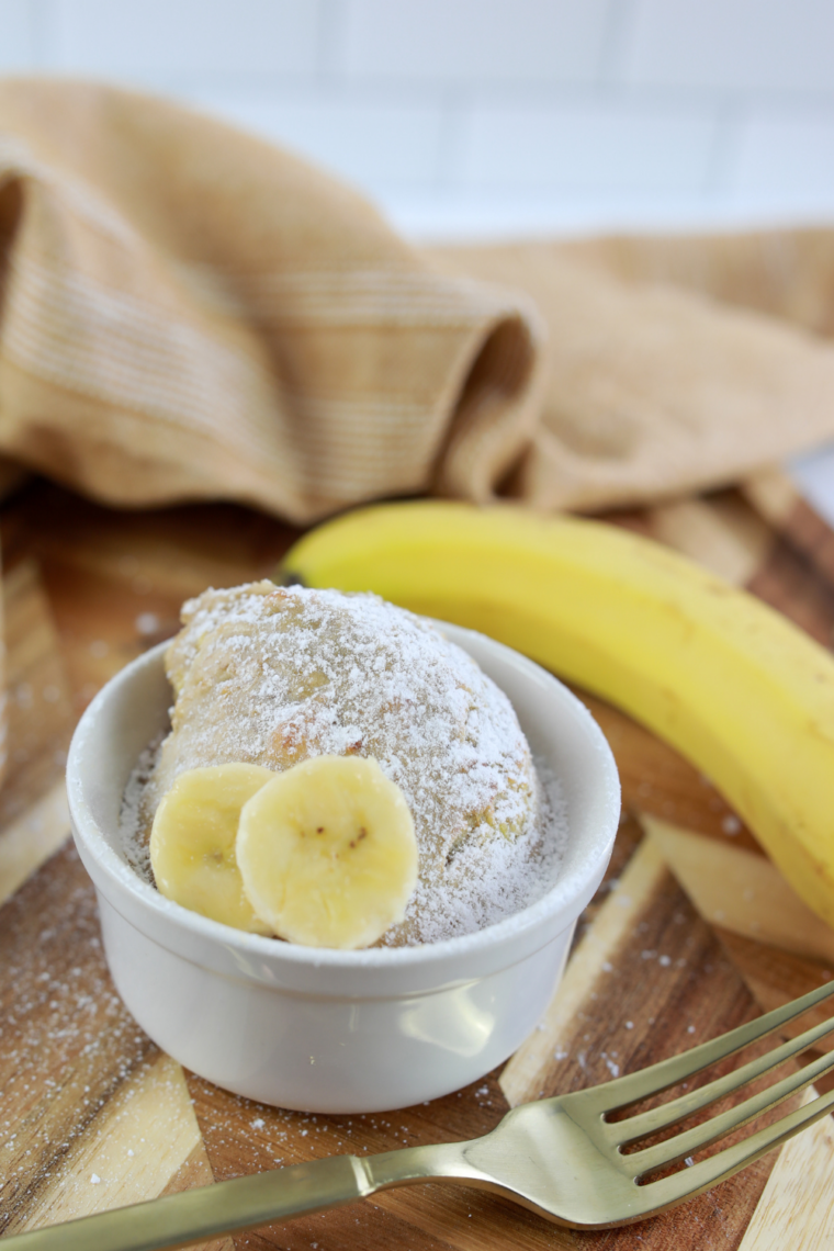 Powdered sugar dusted over a warm banana bread mug cake in a white ramekin 