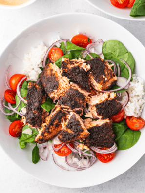 Air fryer blackened salmon fillet with a crispy, dark spice crust, garnished with lemon and fresh herbs on a white plate