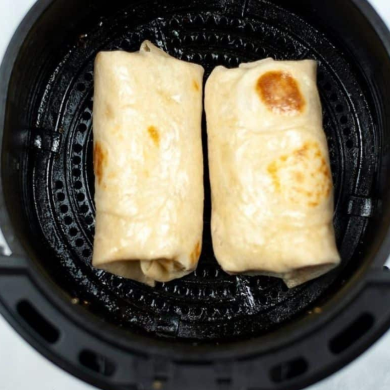 Rolled chimichangas arranged in a single layer in the air fryer basket, ready for cooking.