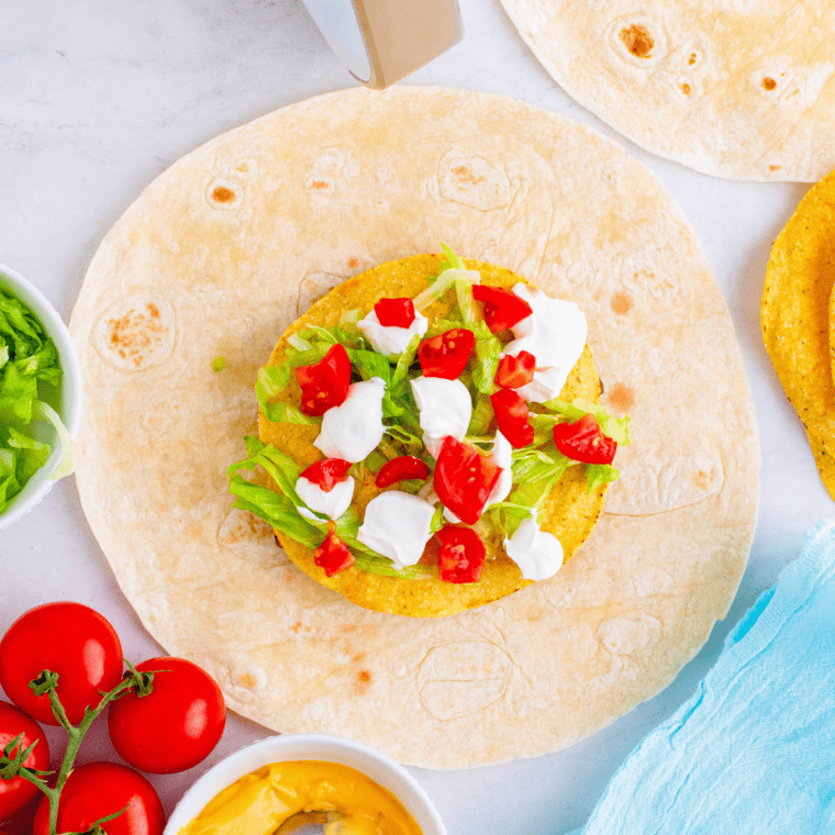 overhead process shot: tostada, lettuce, tomatoes, and sour cream added to large tortilla