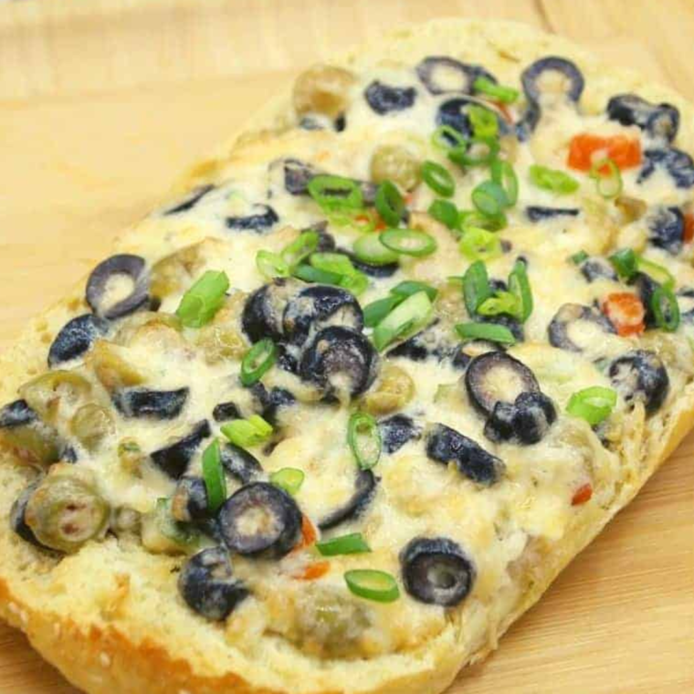 Freshly baked Air Fryer Olive Cheese Bread on a wooden cutting board, garnished with herbs.