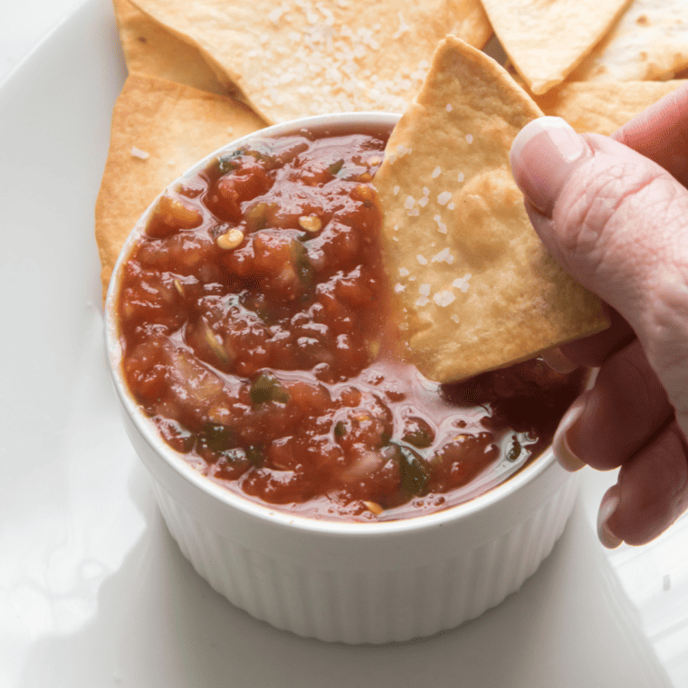 overhead closeup: dipping a tortilla chip into a small bowl of my air fryer roasted salsa recipe