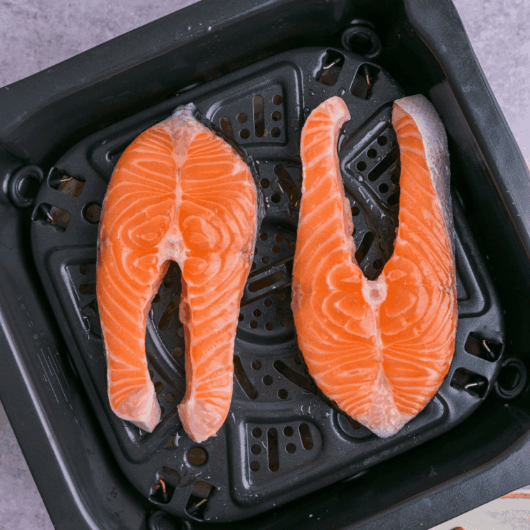 Salmon steaks being patted dry with paper towels, brushed with olive oil, and seasoned with salt, pepper, and garlic powder.