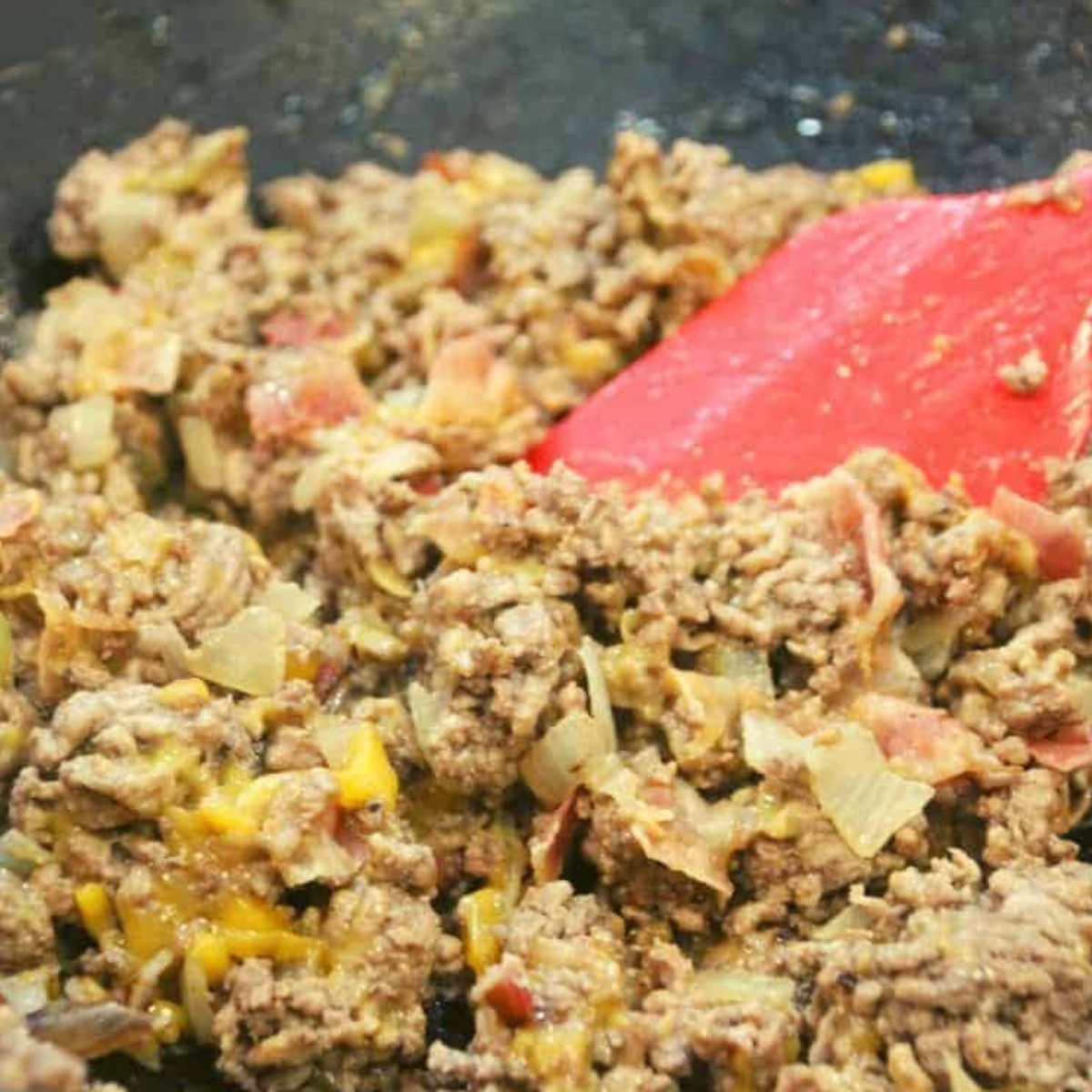Sautéing diced onions and ground beef in a skillet, mixing in shredded cheese, diced cooked bacon, and dill pickles until well combined.