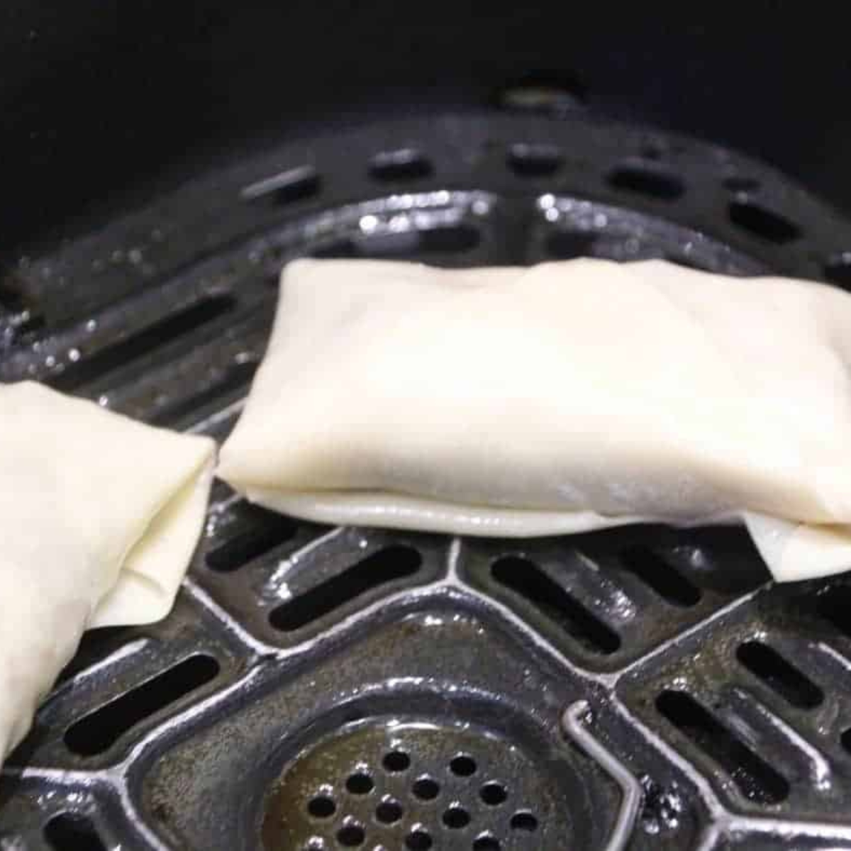 Spraying air fryer basket with nonstick spray and placing homemade egg rolls in a single layer, cooking at 350°F for 8-10 minutes, flipping halfway.