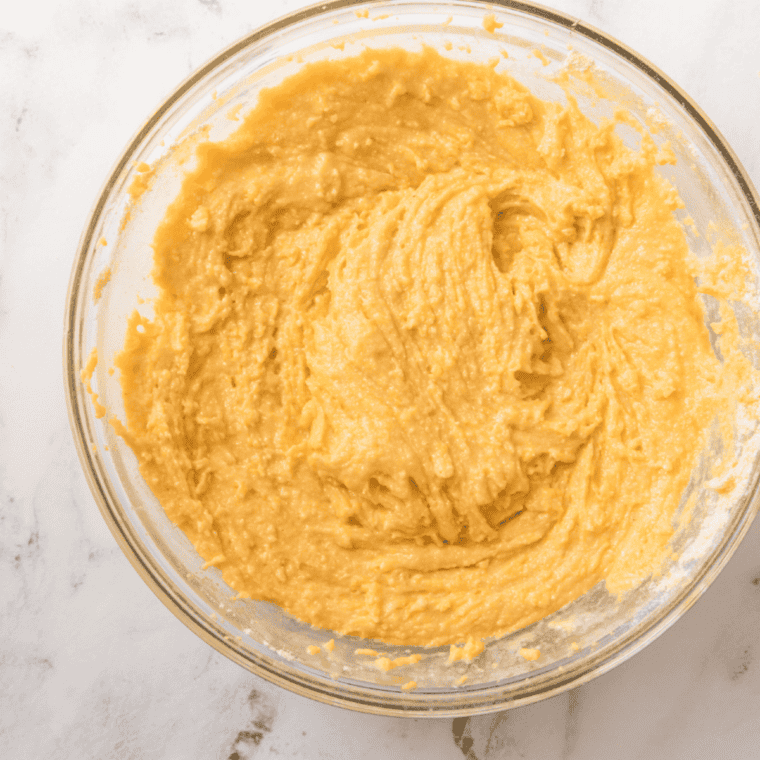 Mixing dry ingredients in one bowl and whisking wet ingredients in another, including milk, eggs, butter, lemon juice, zest, and vanilla for blueberry lemon cornbread batter.