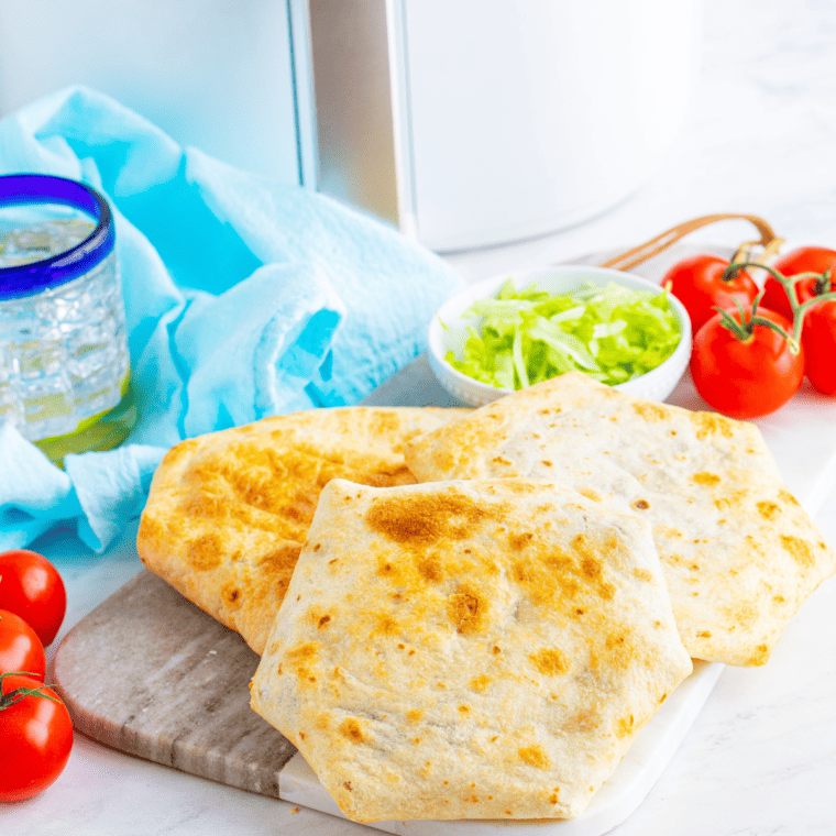 three air fried crunchwrap supremes on a cutting board with lettuce and tomatoes to the side