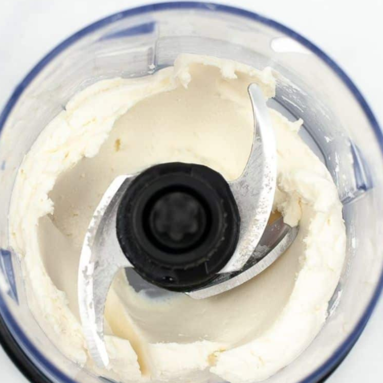 Blending cheese curds in a food processor for smooth, creamy cream cheese with seasonings.