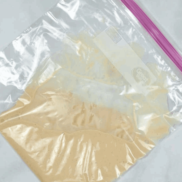 Pouring funnel cake batter into a ziplock bag, cutting a small corner off to pipe into hot oil.
